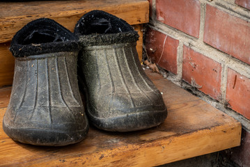 A pair of dirty old black rubber boots (galoshes) on the threshold of the house. Close up.