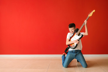 Teenage boy playing guitar against color wall