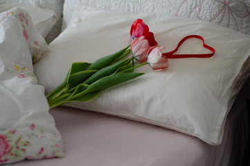 Bouquet of colors tulips and heart on a cozy bed.