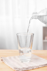 Pouring of fresh water into glass on table
