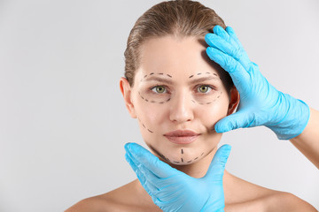 Plastic surgeon touching face of young woman with applied marks on light background