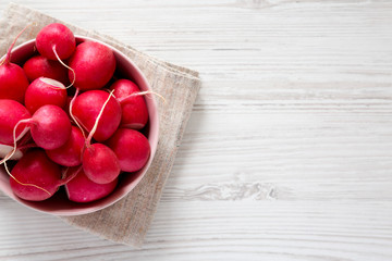 Fresh red radishes in a pink bowl over white wooden background, top view. Flat lay, overhead, from above. Copy space.