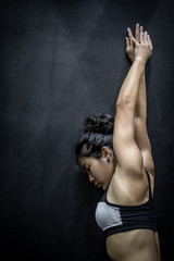 Attractive Asian girl wearing sportswear stretching her arm on black wall in fitness gym. Healthy lifestyle with physical exercise concept.