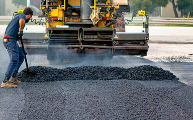 Worker regulate tracked paver laying asphalt heated to temperatures above 160 ° pavement on a runway