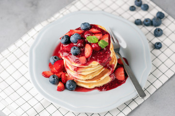 Pancakes with berries and fruit sauce on plate over checkered table textile. Healthy delicious breakfast