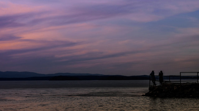Silhouettes of people on dock on the lake at sunset.  Peaceful Lake at Sunset.