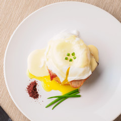 Breakfast is Eggs Benedict - toasted English muffins, bacon, ham, poached eggs, herbs and delicious buttery hollandaise sauce. White plate. Top view . Space for text.