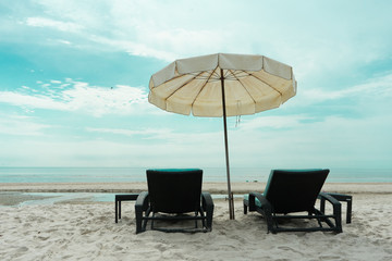 Closeup pair of beach bench on the beach with flying bird in the sky and horizontal skyline above the sea in background