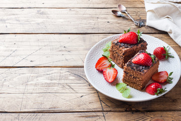 Chocolate truffle cake with strawberries and mint. Wooden table. Copy space