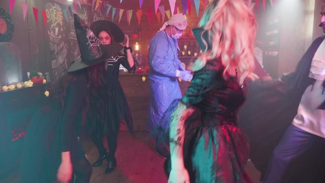 Enchantress in black sensual outfit dancing with her scary friends at a halloween party. Witch, vampire, pirate and mad physician dancing together in a halloween decorated bar.