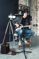 Fototapeta na wymiar Close up of a man singer sitting on a stool in a headphones with a guitar recording a track in a home studio