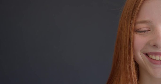 Close-up half face portrait of beautiful ginger model smiling happily into camera on black background.