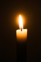 Flame of one white burning brightly wax  candle on the dark black background . Mourning candle. Candle flame