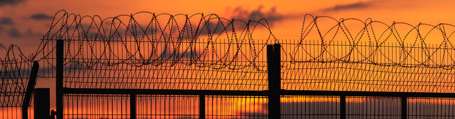 Panorama of a spiny fence on the background of a fiery, bright sunset