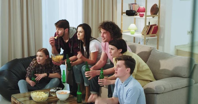 In a modern living room excited group of friends multi ethnic watching on the TV a football match they support their favorite team while drinking some beer