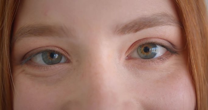 Close-up eye portrait of beautiful ginger model break into a smile in front of camera on white background.