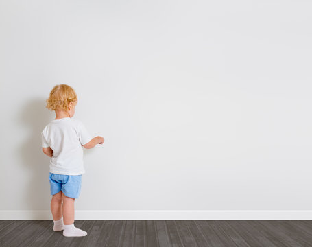 Baby boy drawing on wallpaper standing back to camera