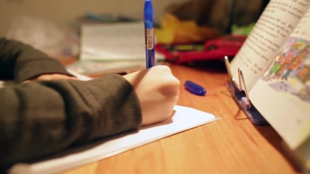 Homework Doer. closeup boy making school homework at home. boy hand with pen, textbook and notebook. boy writes in school notebook, slider shooting forward and back, Dolly Shot