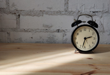 Photo of alarm clock on wooden table against background of brick wall