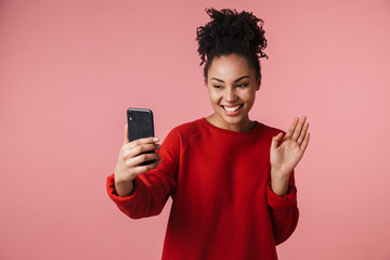Amazing happy excited young african woman posing isolated over pink wall background talking by mobile phone.