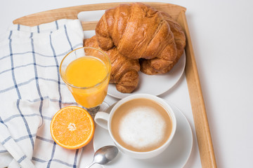 Breakfast coffee with croissants and orange juice on a white background. Latte on a saucer and cellular cotton towel on a wooden tray