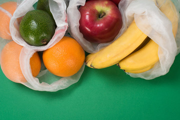Life in the style of zero waste. Fruit orange, apple, avocado, banana in eco bag on a green background. Replacing the plastic bag. Without garbage.
