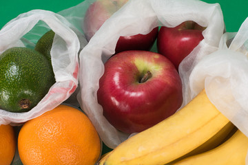 Life in the style of zero waste. Fruit orange, apple, avocado, banana in eco bag on a green background. Replacing the plastic bag. Without garbage.