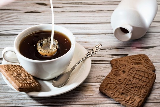 pouring coffee milk with splash in white cup and saucer, traditional dutch cookie speculaas on wooden table
