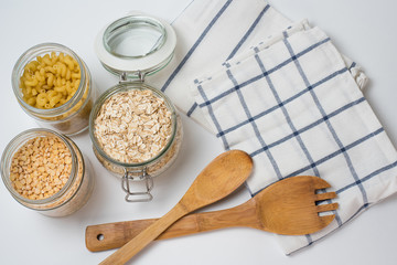 Life in the style of zero waste in the kitchen. Groats (oatmeal, peas, hercules) in a jar, towel and wooden paddles on a white background. Plastic replacement