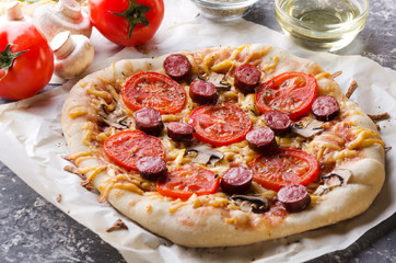Homemade pizza with tomatoes,meat, mushrooms and cheese, fresh vegetables, bowl with oil on the ristic grey table.Closeup of tasty traditional pizza