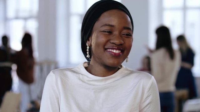Young professional successful African entrepreneur woman wearing ethnic head wrap smiling modestly at modern office.