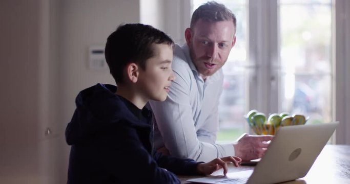 4K Happy teenage boy using laptop at home, chatting & laughing with his father. Slow motion.