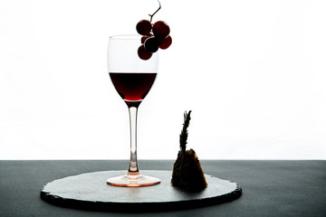 Glass of red wine garnished with grape and piece of hard cheese