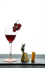 Glass of red wine garnished with grape and pieces of savory cheese