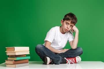 Cute little boy with freckles studying with stack of books