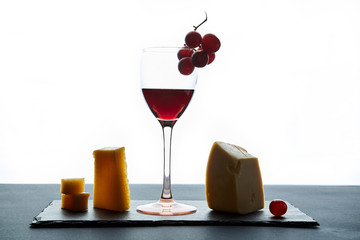 Glass of red wine garnished with grape and different kinds of cheese