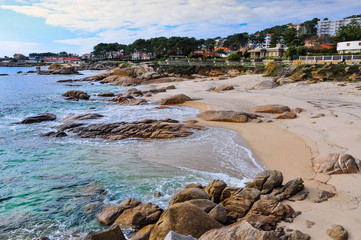 Nice and sunny summer day on the beach, with the sea and the blue sky, houses and apartaments in the background, in Portonovo, Galicia.