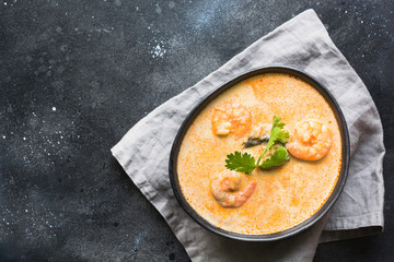 Tom yam kung spicy thai soup with shrimp, seafood, coconut milk and chili pepper in black bowl. Copy space. View from above. Horizontal orientation. Asian cuisine.
