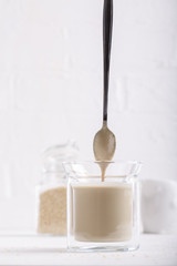 Tahini sauce in glass jar on white background. Natural paste made from sesame seeds.