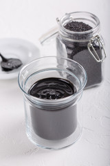 Black tahini sauce in glass jar on white background. Natural paste made from black sesame seeds.