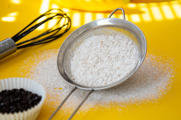 Sieve with flour heaped on yellow background. Creative food concept, baking, recipes.
