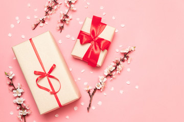 Gift box with red ribbons with a sprig of flowers on a pink background with space for text