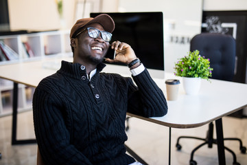 African businessman talking on smartphone and working in office sitting at his workplace.