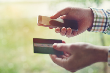 male hands holding credit card and using smartphone, sunny summer day, online shopping concept