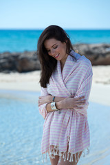 Young girl is on the beach and standing, posing to the camera. Beautiful girl, wrapped in pink...