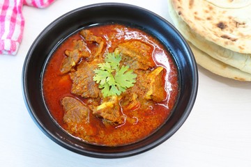 Mutton do Pyaza or Indian lamb Curry with some spices like black pepper, red chili powder, turmeric and garnished with coriander leaves served with Naan or Roti on wooden table