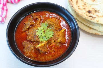 Mutton do Pyaza or Indian lamb Curry with some spices like black pepper, red chili powder, turmeric and garnished with coriander leaves served with Naan or Roti on wooden table