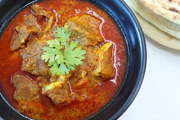 Mutton do Pyaza or Indian lamb Curry with some spices like black pepper, red chili powder, turmeric and garnished with coriander leaves served with Naan or Roti on wooden table