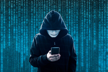 Hooded hacker with mask holding smartphone 