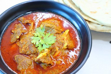 Mutton do Pyaza or Indian lamb Curry with some spices like black pepper, red chili powder, turmeric and garnished with coriander leaves served with Naan or Roti on wooden table